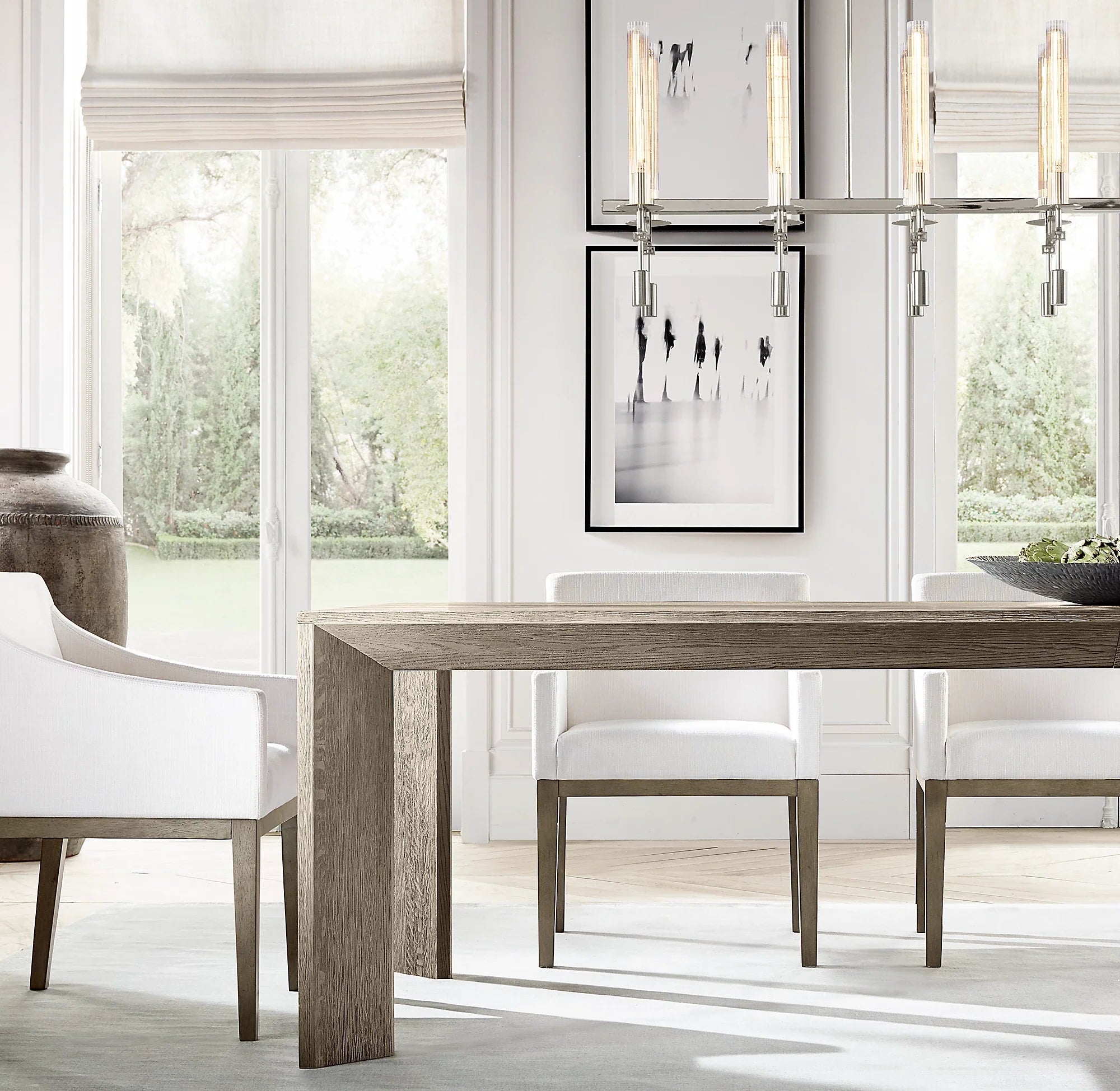Dining room with wooden table and white chairs near large windows.
